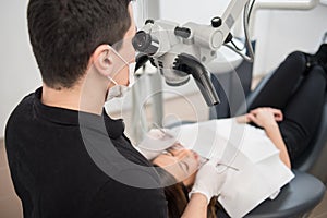 Male dentist with dental tools - microscope, mirror and probe checking up patient teeth at dental clinic office