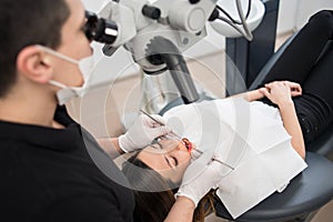 Male dentist with dental tools - microscope, mirror and probe treating patient teeth at dental clinic office