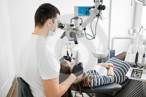 Male dentist with dental tools - microscope, mirror and probe treating patient teeth at dental clinic office