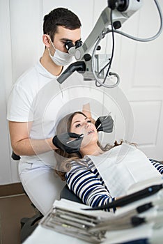 Male dentist with dental tools - microscope, mirror and probe treating patient teeth at dental clinic office