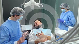 Male dentist discusses treatment with smiling male patient at modern dental clinic. Consultation of a dental surgeon