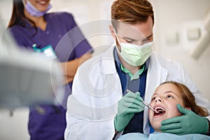 Male dentist examining child`s teeth with dental mirror