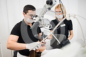 Male dentist and female assistant checking up patient teeth with dental tools. Dental equipment