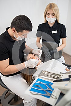 Male dentist and female assistant checking up patient teeth with dental tools at dental office. Medicine, dentistry