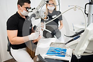 Male dentist and female assistant checking up patient teeth with microscope at dental clinic office. Dental equipment