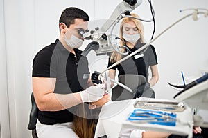 Male dentist and female assistant treating patient teeth with dental tools - microscope, mirror and drill