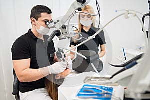 Male dentist and female assistant treating patient teeth with dental tools - microscope, mirror and drill