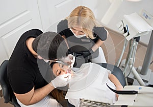 Male dentist and female assistant treating patient teeth with dental tools - mirror and probe at dental clinic office