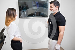 Male dentist with female patient against dental x-ray image on computer monitor in the dental office