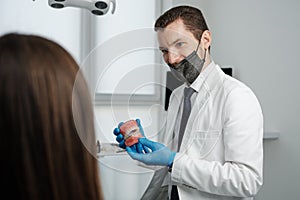 Male dentist holding tooth model with metal braces and speaks to his patient