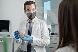 Male dentist holding tooth model with metal braces and speaks to his patient