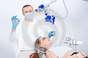 A male dentist in mask and a patient woman in the dentist chair. Male dentist examining patient looking on the teeth with