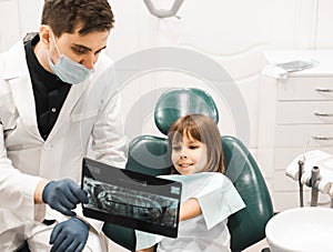 male dentist showing teeth x-ray to child girl at dental clinic office