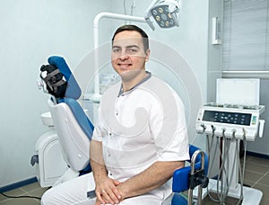 Male dentist sitting on background of dentists chair in dental clinic