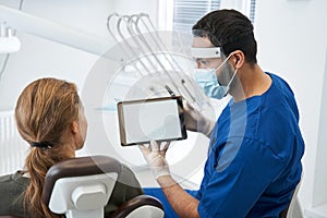 Male dentist talking to his woman patient in dentist surgery