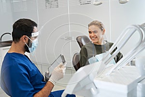 Male dentist talking to his woman patient in dentist surgery