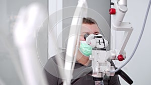 Male dentist treating patient using microscope in modern dentistry office. Doctor works with microscope, installs