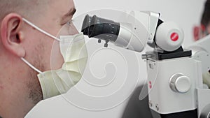 Male dentist working with dental microscope in modern dentistry clinic. Endodontist looking in microscope during the