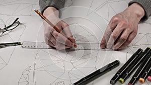 Male designer makes a working drawing. Workplace of a toy designer. Markers, ruler, pen and pencil are on the drawing