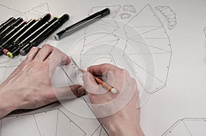 Male designer makes a working drawing. Workplace of a toy designer. Markers, ruler, pen and pencil are on the drawing