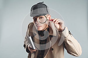 Male detective looking through magnifying glass on grey background