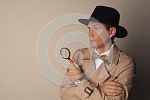 Male detective with magnifying glass on beige background. Space for text