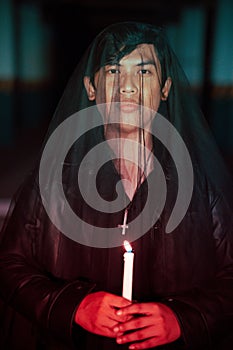 a male devil worshiper with a transparent veil is performing a spooky ritual by holding a candle in his hand