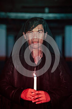 a male devil worshiper with a transparent veil is performing a spooky ritual by holding a candle in his hand photo