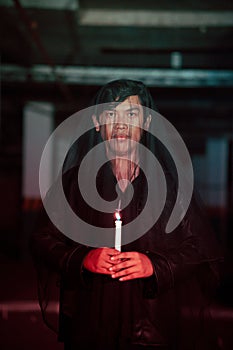 a male devil worshiper with a transparent veil is performing a spooky ritual by holding a candle in his hand photo