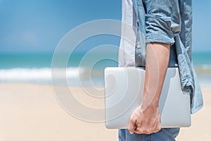 Male digital nomad hand holding laptop on the beach