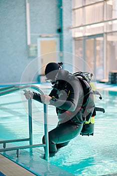 Male diver in scuba gear climb out of the pool