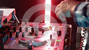 Male DJ hands composing music mix console controller at night party illuminated nightclub closeup