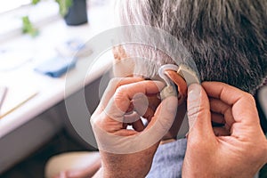 Male doctor applying hearing aid to senior woman
