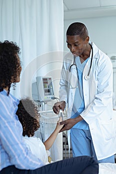 Male doctor attaching pulse oximetry on child patient hand in the ward