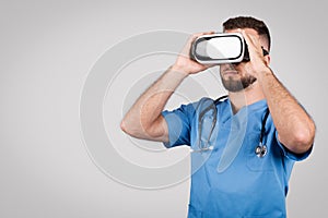 Male doctor in blue using VR glasses, grey background, copy space