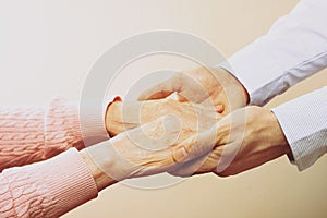 Mature female in elderly care facility gets help from hospital personnel nurse. Close up of aged wrinkled hands of senior woman. G