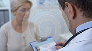 Male doctor checking female patient medical history form, health examination