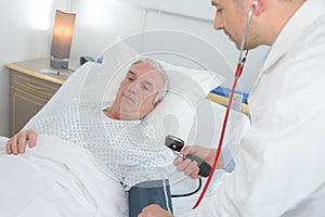 male doctor checking senior mans blood pressure in hospital