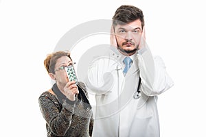 Male doctor covering ears and female patient showing pills