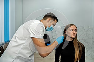 male doctor or ENT specialist examining the ear with an endoscope with patient in his practice.