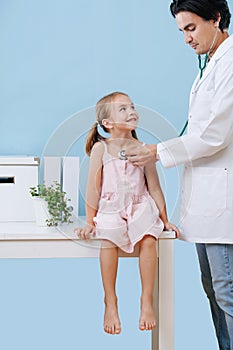 Male doctor examining a cheerful child girl, that sits on a table in a hospital