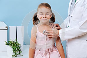Male doctor examining a cheerful child girl, that sits on a table in a hospital