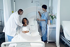 Male doctor examining female patient with stethoscope in the ward