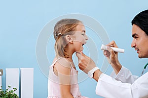 Male doctor examining little girl`s tonsils at hospital, using flashlight