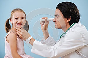 Male doctor examining little girl`s tonsils at hospital, using flashlight