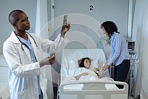 Male doctor examining x-ray report while mother holding her sons hands in the ward