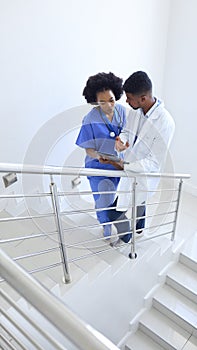 Male Doctor And Female Nurse With Digital Tablet Discussing Patient Notes On Stairs In Hospital