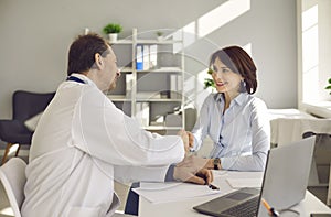 Male doctor greeting handshaking smiling female patient in hospital office