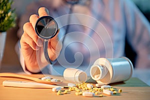 Male doctor hand holding stethoscope over pills on the desk