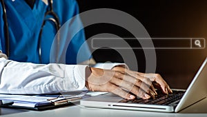 Male doctor hands typing on laptop computer keyboard,searching medical information with textbook on the desk at office.